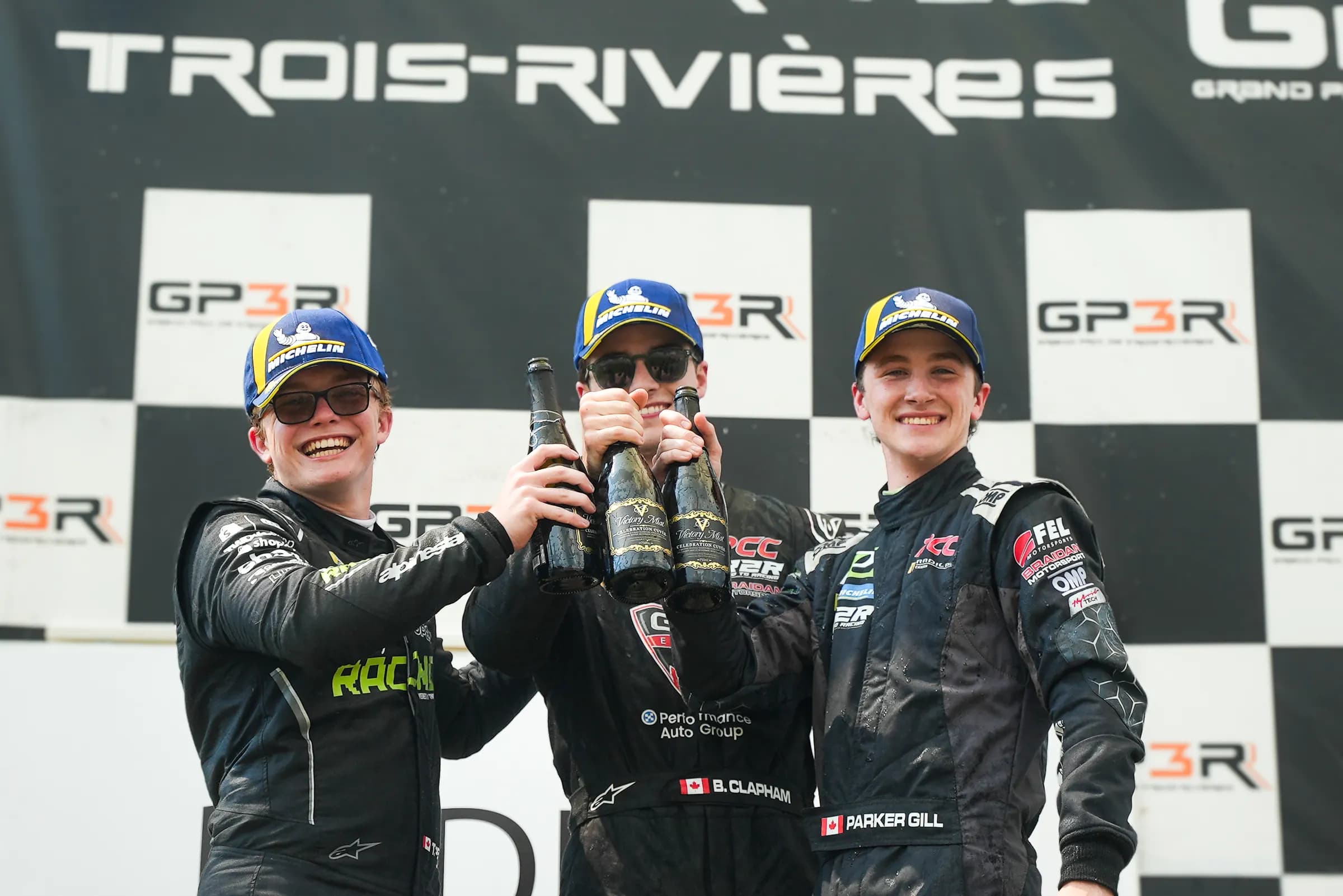 Three drivers on a podium raising bottles of Victory Mist to each other